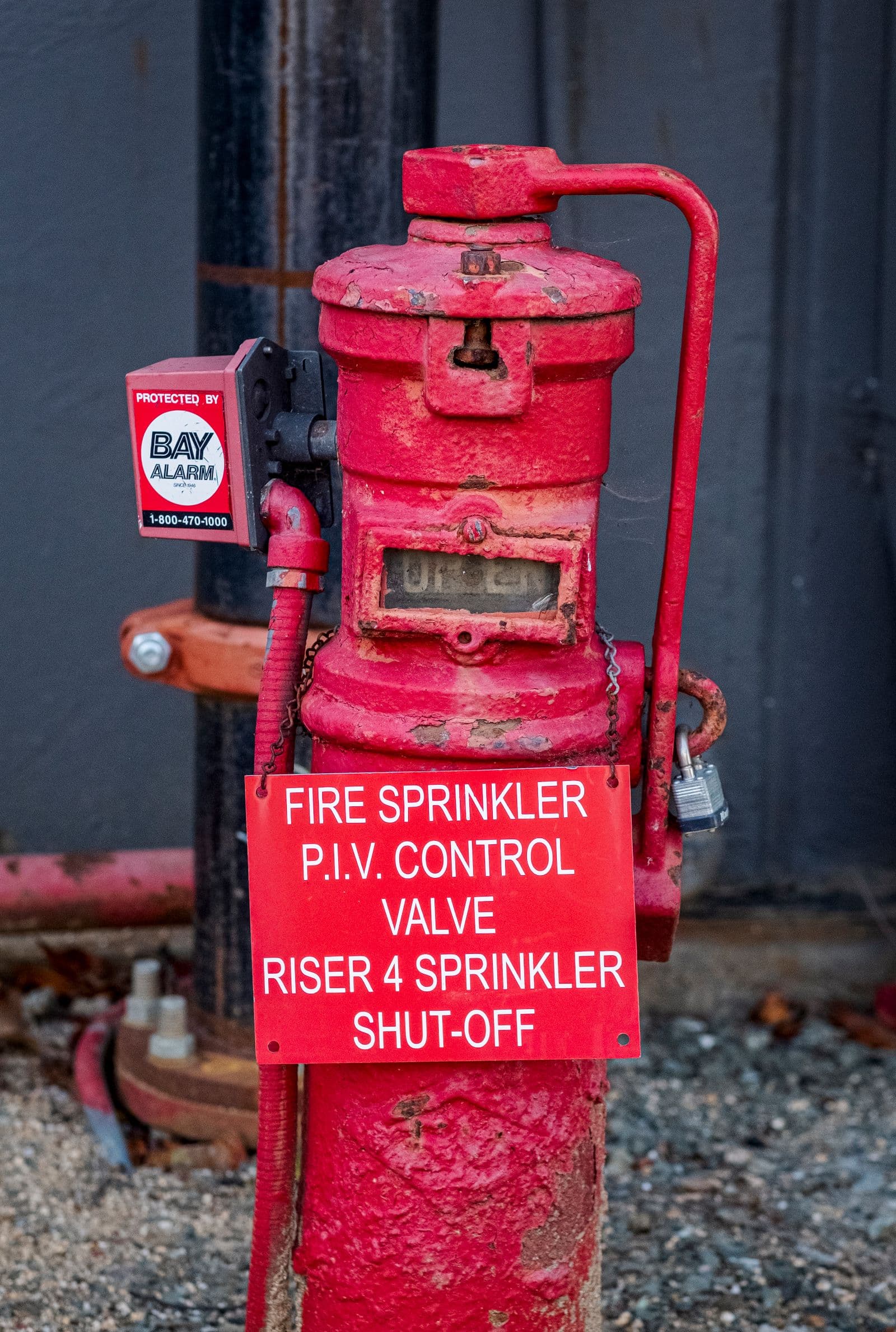 Red fire-sprinkler post-indicator control valve on a commercial building riser, tagged and locked for shut-off